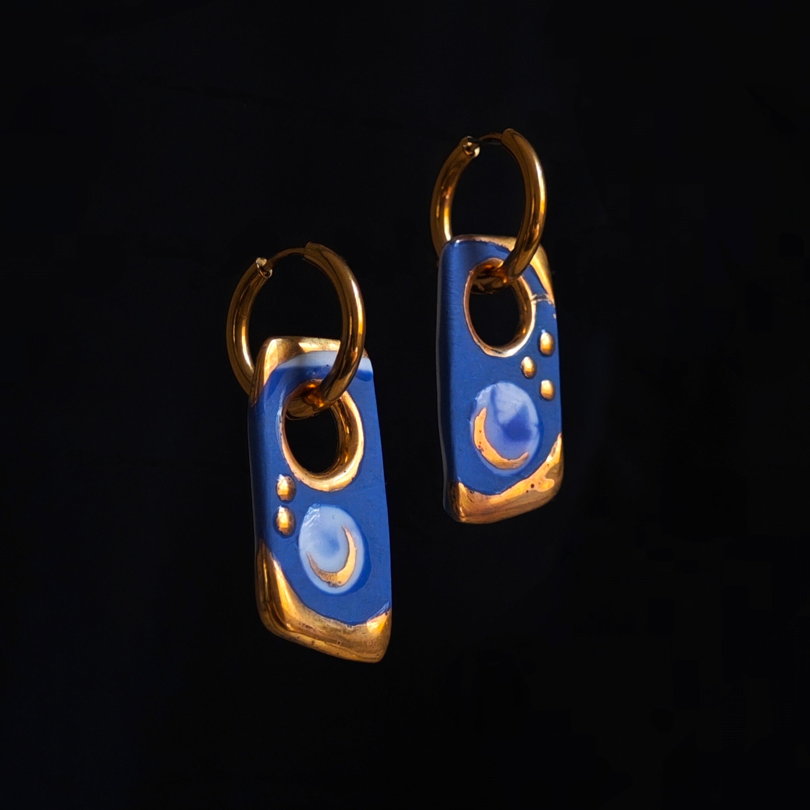 Pair of blue and gold earrings on a black background